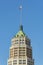 Towering skyscraper in afternoon sun with green copper top and cement exterior facade with round design in blue sky