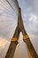 A towering suspension bridge, with concrete pillars and steel cables, stands against a cloudy sky