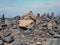 Towers of stacked pebbles and stones in different colours in a large arrangement on a black sand beach with blue sky