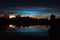 Town view of noctilucent clouds NLC. Beautiful waves and ripples of silver blue night shining clouds over some houses in summer