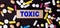 TOXIC is written on a wooden block next to multi-colored pills on a dark table. Medical concept