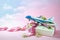 Toy airplane on a gift box with ribbon and some flowers, pink background fading into a cloudy blue sky, travel and journey present