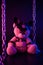 Toy bear dressed in leather belts harness accessory for BDSM games on a dark background in neon light