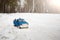 A toy. Blue pickup truck in winter forest with open door on the road. Carrying fir cones in the back of a car body