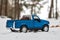 A toy. Blue pickup truck in winter forest on the road. Carrying fir cones in the back of a car body