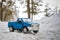 A toy. Blue pickup truck in winter forest on the road. Standing with open door