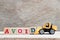 Toy bulldozer hold block d to complete word avoid on wood background