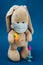 Toy bunny with thermometer under paw and in mask, syringe on a blue background