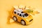 Toy car bursts through torn paper, autumn on yellow paper. The concept of a cozy and modern autumn. Trend yellow