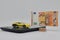 A toy car stands on an electronic scale next to a stand with a banknote, the concept of determining the cost of a car when selling