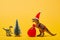 Toy dinosaurs with santa hat and sack beside pine