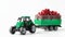 Toy farm tractor transports red fresh cranberries in a cargo trailer. White background. Concept of agricultural work and