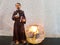 Toy figure of saint Francis holding a white dove bird and a bible next to a burning candle