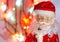 Toy, figurine, Santa Claus. Toy Santa Claus on the background of garland lights. Face, parts of the body of Santa Claus. New Year