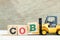 Toy forklift hold block B to complete word COB abbreviation of close of business on wood background