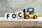 Toy forklift hold block c to complete word FOC Abbreviation of Free of charge on wood background