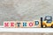 Toy forklift hold block d to complete word method on wood background