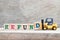 Toy forklift hold letter block D to word refund on wood background