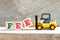 Toy forklift hold letter block e to word fee on wood background