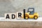 Toy forklift hold letter block r to complete word ADR Abbreviation of Adverse drug reaction on wood background