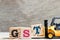 Toy forklift hold letter block T to word GST abbreviation of Goods and Services Tax on wood background