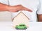 Toy green car and house miniature covered by man hand. Property protection and insurance concept.