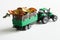 Toy green tractor takes out dry fallen autumn leaves in a trailer. Agricultural work concept. Selective focus. White background.