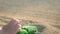 A toy green truck is riding along the sand.