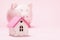 Toy house and piggy bank on a pink background with copy space. Concept of accumulating money to buy a house