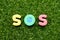 Toy letter in word SOS abbreviation of save our soul/ship or sibling over shoulder on green grass background