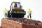 Toy pavement roller and construction workers on chocolate biscuit cake with chocolate chips. Concept of construction, exploration