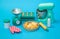 toy plastic cooking machine to prepare dough, bottle of milk, rolling pin, scales, eggs, oven glove and finished cakes on blue