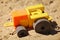A toy plastic tractor on the sand of a playground.
