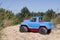 Toy red blue pickup in the sand of a green forest background.