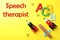 Toy rockets and school supplies and text Speech Therapist on yellow background, flat lay