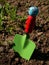 Toy shovel with green blade and ladybug handle jabbed in garden soil