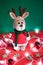 Toy small Christmas deer on a red and green background with decorations and lights from a garland. Cute handmade knitted deer in a