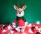 Toy small Christmas deer on a red and green background with decorations and lights from a garland. Cute handmade knitted deer in a