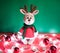 Toy small Christmas deer on a red and green background with decorations and lights from a garland. Cute handmade knitted deer in a