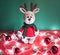 Toy small Christmas deer on a red and green background with decorations and lights from a garland. Cute handmade knitted deer in a