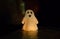 A toy smiling ghost stands in the dark and is illuminated by a reddish light
