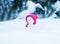 Toy snowman in a bright pink cap sitting in a white snowdrift with a gift