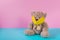 Toy Teddy bear wearing yellow mask on its face and sitting on colorful floor. Copy space. Concept of protecting children during a