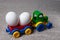 A toy tractor carries two chicken eggs. Plastic and natural food.