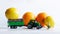 Toy tractor and little man harvest lemons and oranges on a white background. A playful concept of a giant harvest in a toy world.