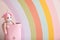 Toy unicorn in basket near wall with painted rainbow, space for text. Interior design