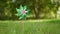 Toy windmill green pink shiny color turns in the wind on nature outdoor on a background of green grass on a Sunny summer day. Nois