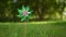 toy windmill green pink shiny color turns in the wind on nature outdoor on a background of green grass on a Sunny summer day. Nois
