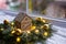 Toy wooden winter house near fir wreath decorated with golden Christmas balls and coiled with glowing garland with warm light on w