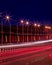 Traces of headlights from cars moving at night on the bridge, illuminated by lanterns. Abstract cityscape with highway at dusk